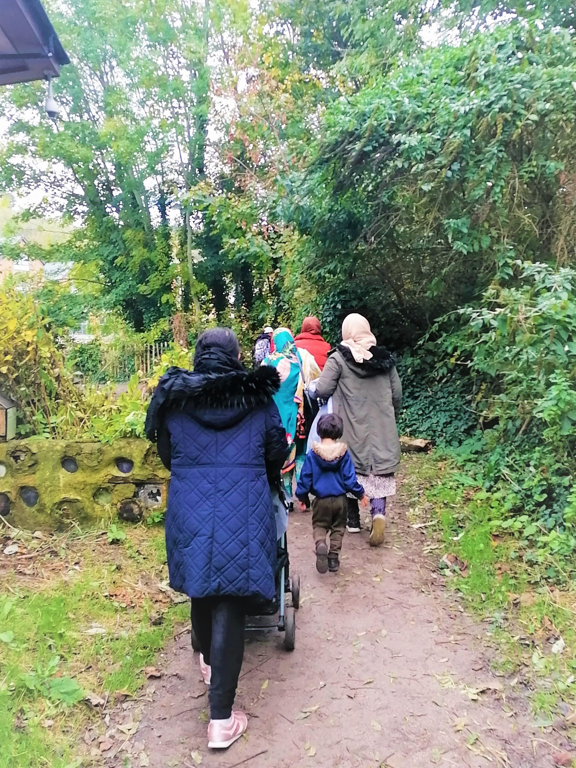 A group of women and children walk along a woodland path.