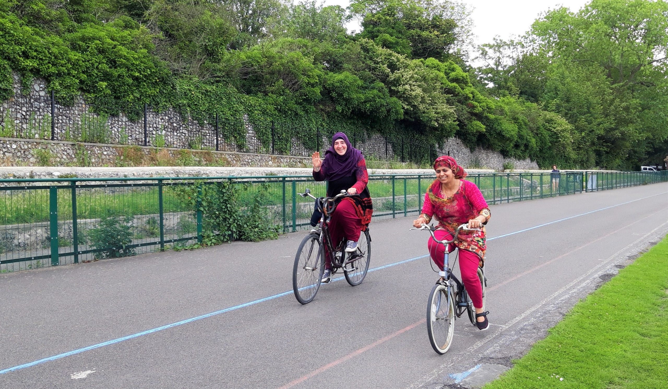 Two women cycle around preston park. One of them waves.